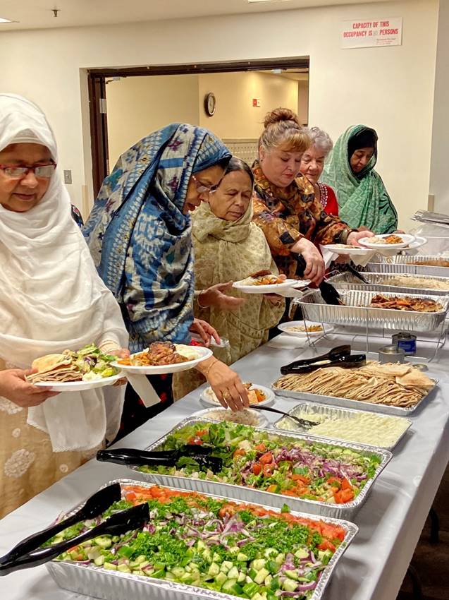 A group of women getting mediterranean food down an assembly line.