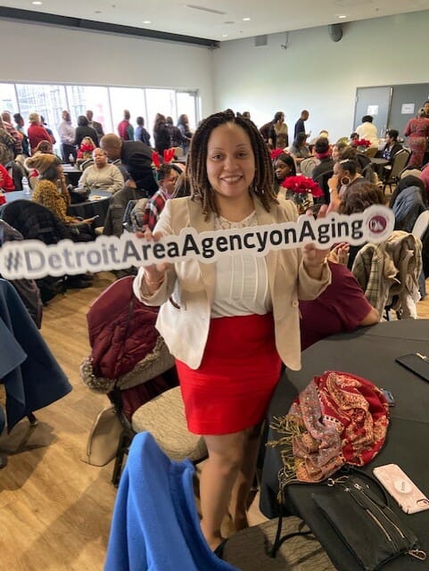 A woman standing at an event holding a Detroit Area Agency on Aging sign | Quality and Compliance landing page