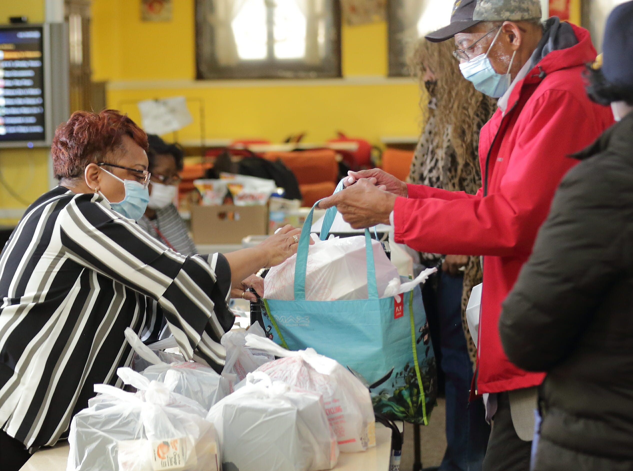 A woman is helping a man placing food carryouts in his reusable bag