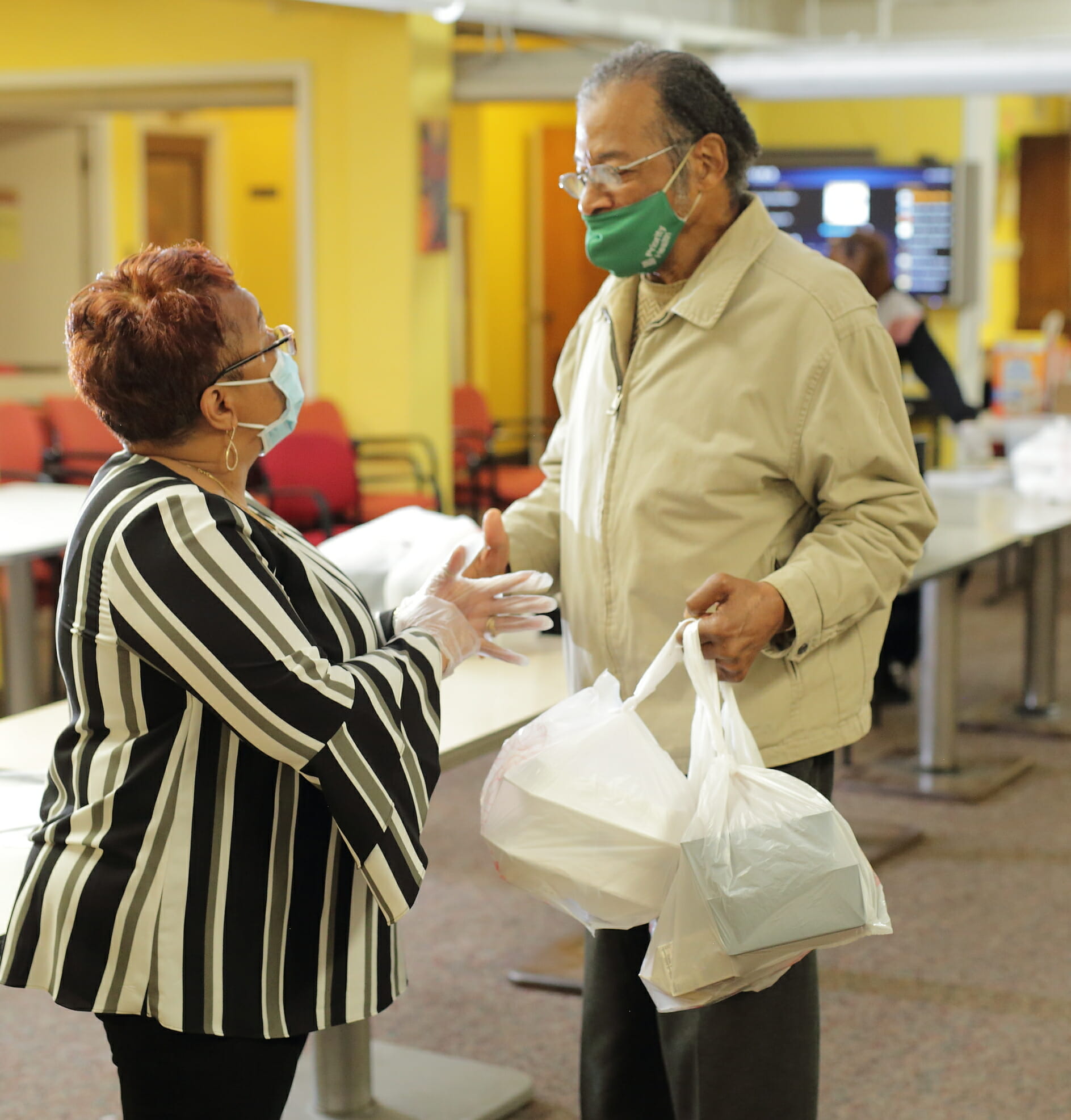 A woman talking to a man who is carrying multiple bags with food carryout containers