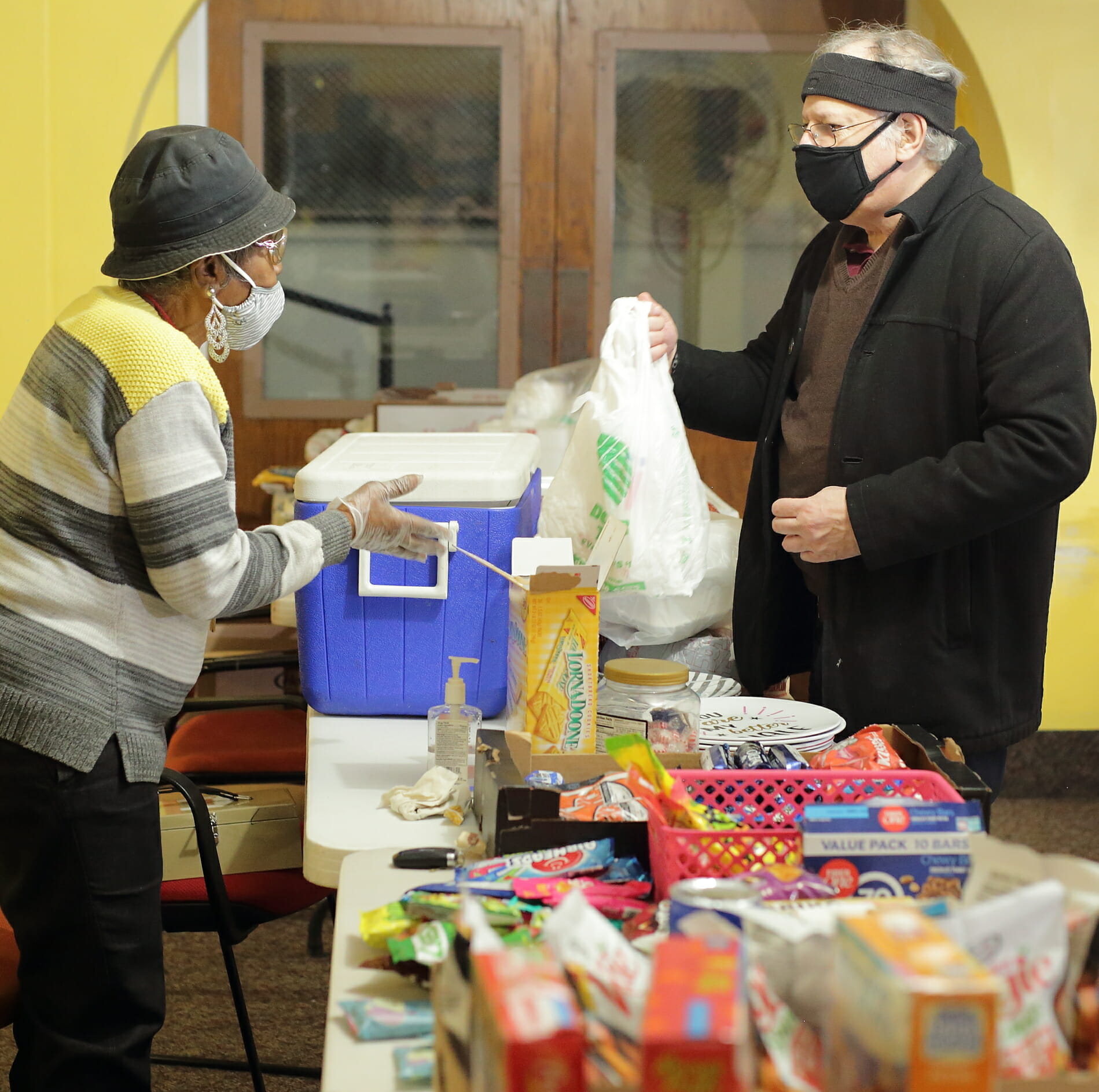 A woman is talking to a man who is holding a bag - both are wearing protective masks.